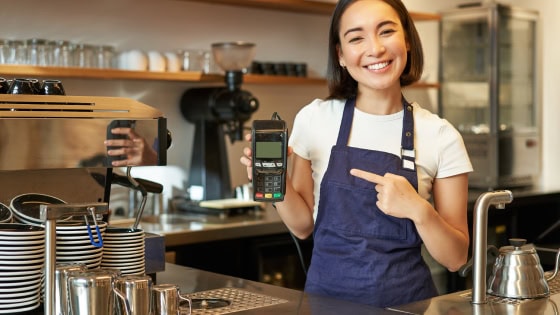 A barista in a blue apron showcases a POS system for seamless payment processing.