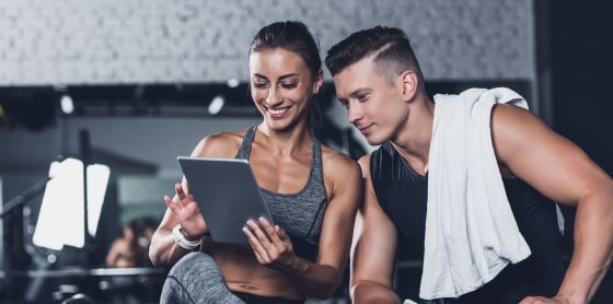 Two people in athletic wear at a gym, discussing a POS system on a tablet.