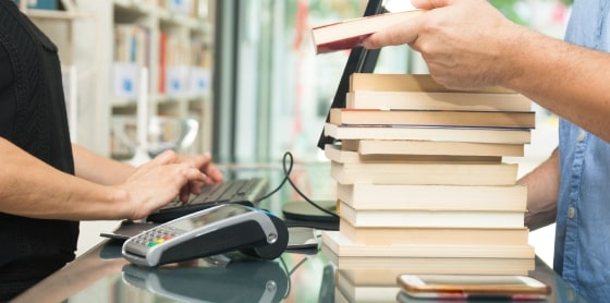 Person buying books at POS with smartphone and merchant services payment gateway.