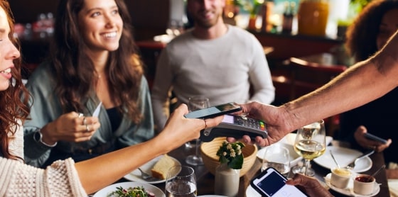People at a restaurant table, using POS system for contactless credit payment.