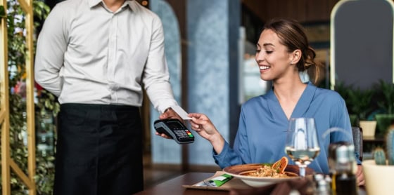 A woman processes her credit card via a POS system at a restaurant table.