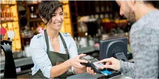 A cashier hands a POS terminal to a customer for secure merchant payment processing.